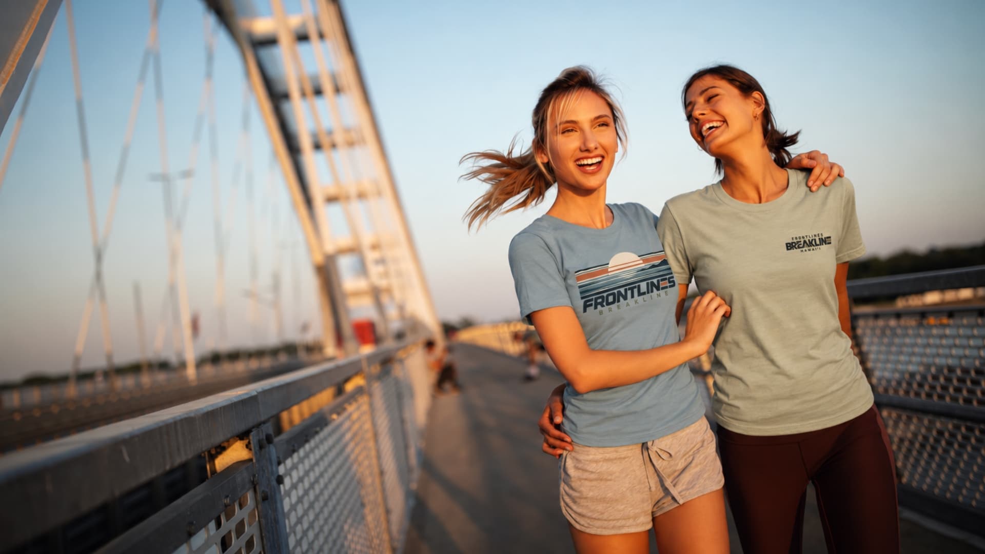 Two women wearing Breakline apparel on a bridge at golden hour