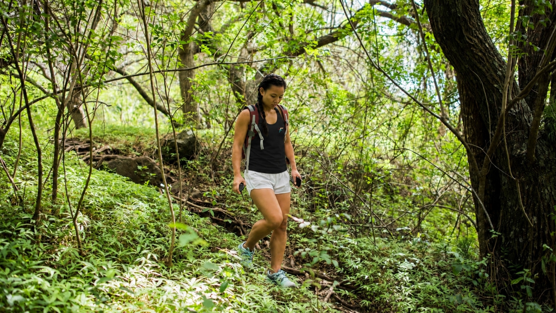 A woman hiking a forest trail in a black Frontlines Performance tank