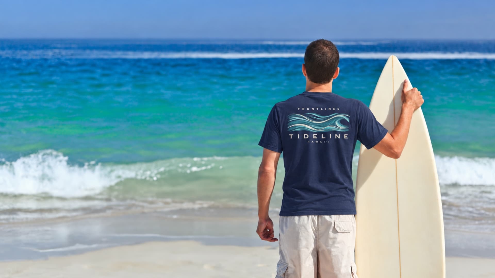 A surfer wearing a navy Frontlines Tideline tee beside the ocean