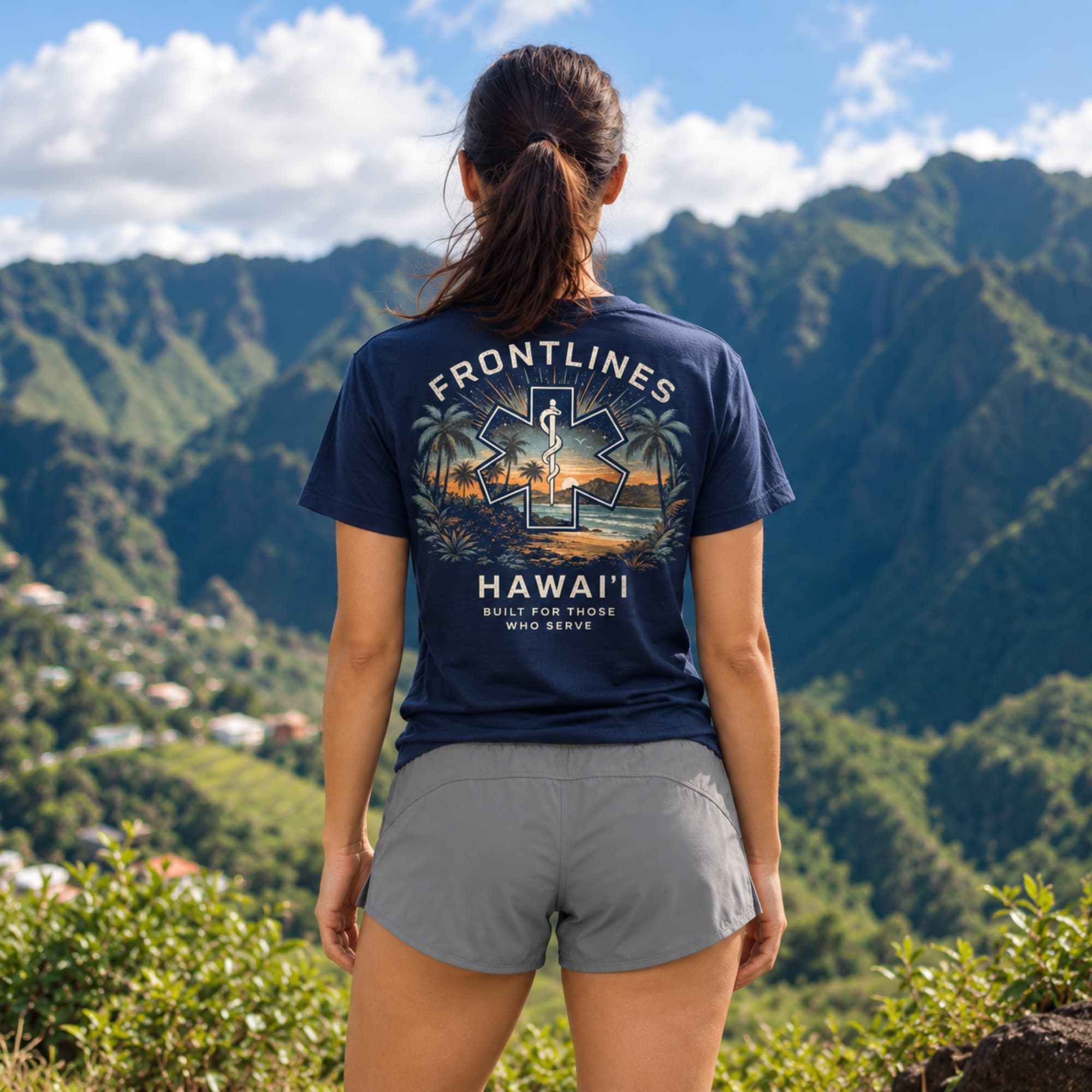 Woman wearing a navy Frontlines Hawaiʻi EMS graphic tee overlooking green island mountains